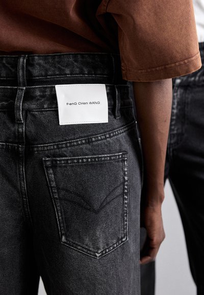 Black denim jeans featuring a distinct back pocket design, a white label with "Feng Chen Wang," and a slightly faded texture.