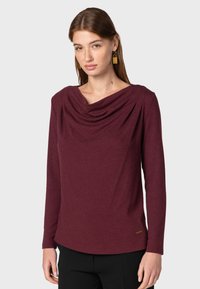 Długi rękaw bluzka w głębokim burgundowym kolorze z luźnym dekoltem typu cowl i zaokrąglonym dołem. Wykonana z miękkiego materiału z minimalnymi detalami przeszycia.
