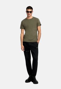 Tricou verde măsliniu cu guler rotund, asortat cu pantaloni de trening negri cu șnururi și detalii cu logo. Botine negre chunky completează look-ul.