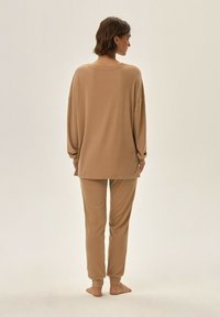 Beżowy zestaw odzieży domowej składający się z luźnego topu z długim rękawem oraz zwężających się spodni, oba z miękkiej tkaniny i z mankietami na kostkach.