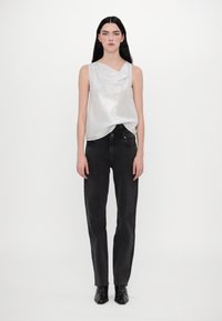 Top sans manches argenté avec un col drapé, associé à un jean noir taille haute. Le mannequin porte des bottines noires. Design simple et épuré.