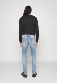 Sudadera negra de mangas largas, combinada con jeans ajustados de color azul claro y calzado negro. Tejido suave con un diseño simple y minimalista.