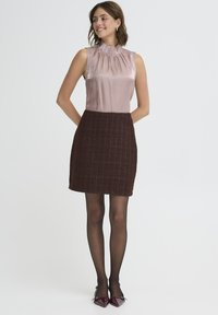 Top senza maniche in satin leggero color malva, con colletto arricciato, abbinato a una mini gonna textured marrone scuro. Collant neri trasparenti e tacchi borgogna.