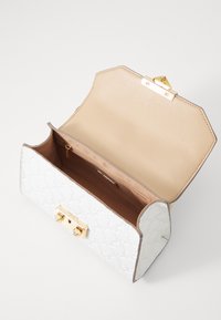 Bolso blanco con estampado, con herrajes dorados, de forma octogonal y con un interior marrón claro. Presenta un cierre seguro y un bolsillo con cremallera en el interior.