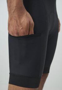 Shorts de sport noirs avec une texture lisse, dotés d'une poche latérale pour le rangement et d'une coupe ajustée qui met en valeur la forme des jambes.