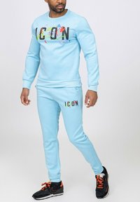 Ensemble sweatshirt et joggers bleu ciel avec impression "ICON" en noir et éclaboussures colorées. Doté de poignets côtelés et d'un design slim-fit.
