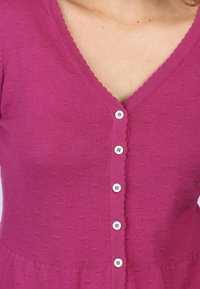 V-neck knit cardigan in bright pink with subtle textured pattern, featuring five white buttons down the front and scalloped edges.