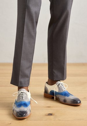 Des derbies en cuir alliant des tons de gris, bleu et crème avec des perforations et des lacets blancs, assorties à un pantalon gris tailleur.