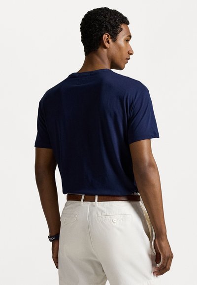 Tricou din bumbac de culoare albastru marin, cu mâneci scurte, guler rotund și croială lejeră, asortat cu pantaloni bej deschis și o curea din piele maro.