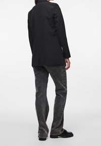 Czarna, dopasowana marynarka o strukturalnym kroju, zestawiona z ciemnoszarymi dżinsami o delikatnym wyblaknięciu oraz czarnym obuwiem na masywnej podeszwie.