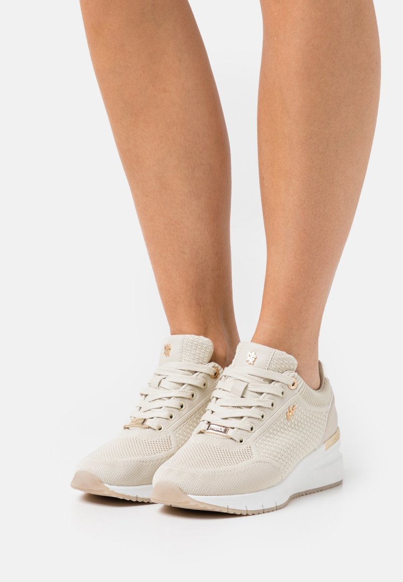Béžové sportovní boty s texturovaným síťovaným svrškem, plochými tkaničkami a bílou podešví. Zlaté akcenty na dírkách na tkaničky a bočním detailu.