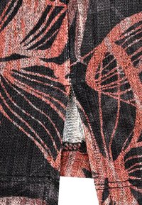 Stricktop mit einem schwarzen und korallenfarbenen Blumenmuster. Verfügt über ein strukturiertes Design, sichtbare Nähte und eine kleine Öffnung am Saum.