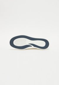 Sole di sneaker bianca con accenti in gomma blu, superficie testurizzata e motivi perforati per aderenza. Finitura liscia con design curvo.