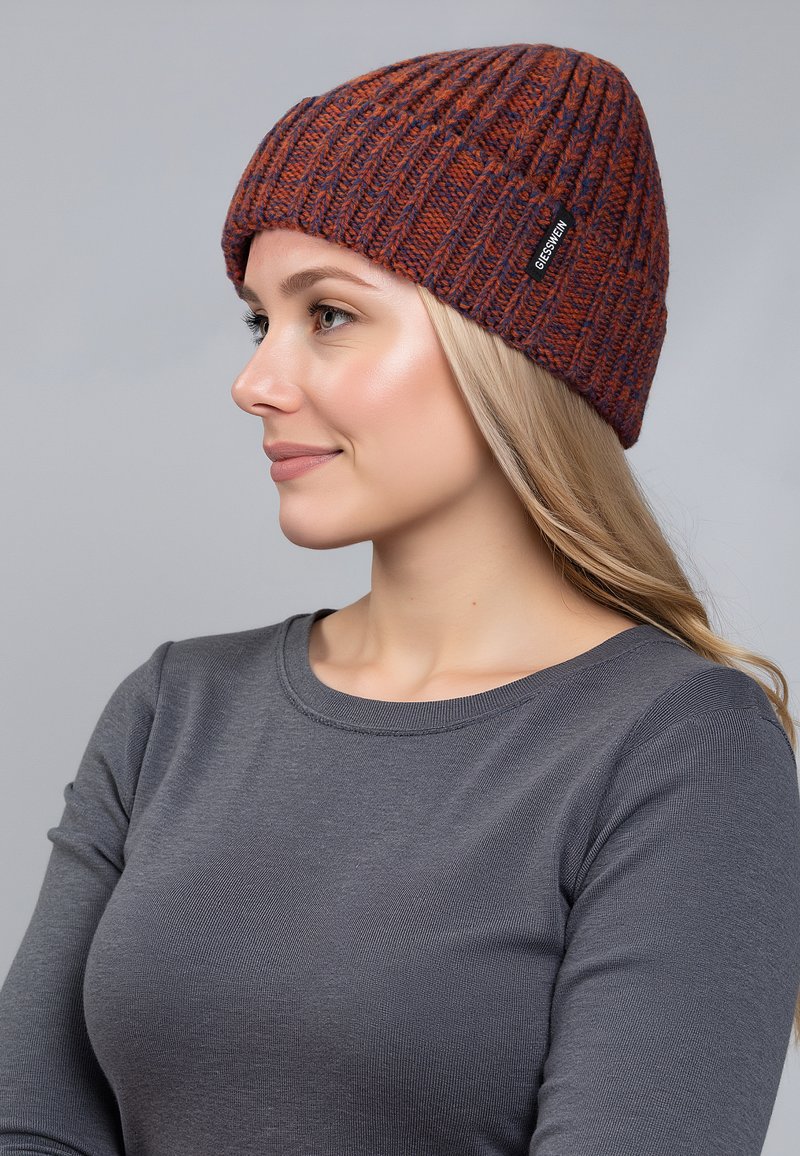 Gehaakte beanie in oranje en paarse tinten, met ribbeltextuur, voorzien van een zwart logo-label. Model draagt een grijze longsleeve.