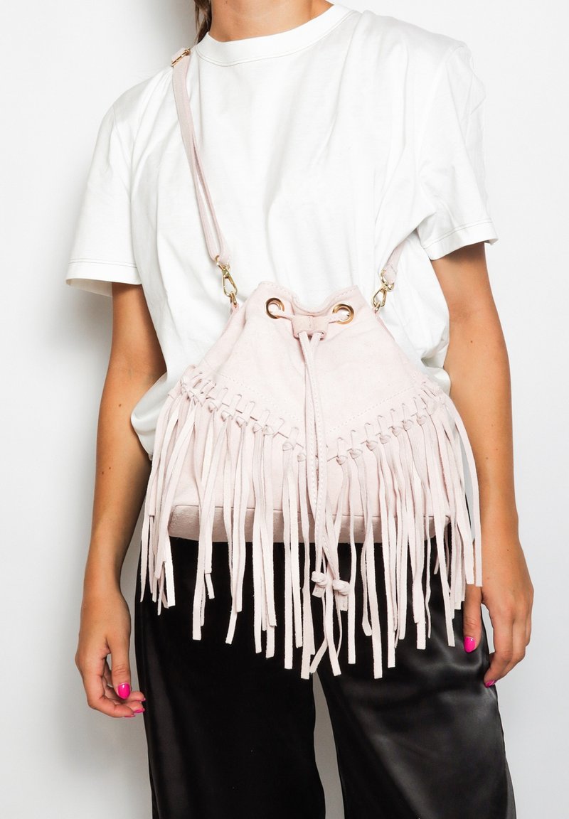 Borsa a tracolla in suede rosa con dettagli in frange, chiusura a cordoncino e accessori in oro. Indossata a tracolla con cintura regolabile.