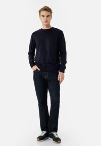 Navy gebreide trui met lange mouwen, ronde hals, gecombineerd met donkerdenim jeans en zwarte sneakers met witte veters.