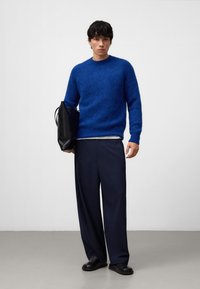 Niebieski puszysty sweter, ciemnoniebieskie szerokie spodnie i czarna torba. Strój składa się z teksturowanego swetra i gładkiej skórzanej torby.