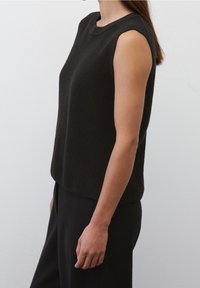 Top nero senza maniche in maglia con superficie texturizzata e scollo rotondo, abbinato a pantaloni neri, mostrato da un'angolazione laterale.