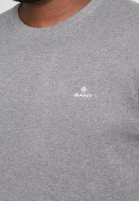 Maglione grigio lavorato a maglia con scollatura tonda e tessuto testurizzato. Presenta un piccolo logo bianco sul petto.