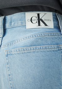 Poche arrière d'un jean en denim bleu clair avec une étiquette blanche rectangulaire Calvin Klein Jeans cousue au-dessus de la poche.