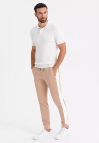 Witte geribbelde polo shirt gecombineerd met beige joggers met witte zijstreep, afgemaakt met witte sneakers. Minimalistisch, getailleerd ontwerp.