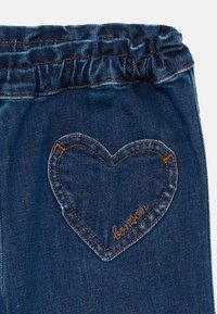 Jeans de mezclilla con una cintura elástica ajustada. Presenta un contorno de bolsillo en forma de corazón con costuras naranjas en contraste y la palabra "bonton."
