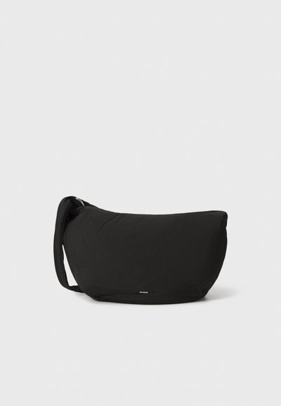 Borsa a spalla in tessuto nero con forma curva, cinturino regolabile e chiusura con zip. Presenta un discreto dettaglio del logo nella parte anteriore.