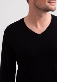 Schwarzer V-Ausschnitt-Pullover mit langen Ärmeln, aus weichem Stoff gefertigt. Verfügt über einen gerippten Kragen und eine glatte, strukturierte Oberfläche.