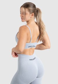 Sujetador deportivo azul claro y leggings de tiro alto hechos de tela elástica. Presenta acentos de logo y una textura acanalada. Diseño sin costuras.