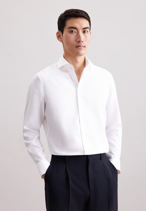Witte textuur blouse met een puntig kraag, knoopsluiting aan de voorkant en lange mouwen; gecombineerd met donkere, op maat gemaakte broeken.