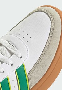 Bijela tenisica s gornjim dijelom od teksturirane kože, zelenim i neonski žutim bočnim trakama, svijetlo sivim suedenim panelom i smešnim gumiranim potplatom.