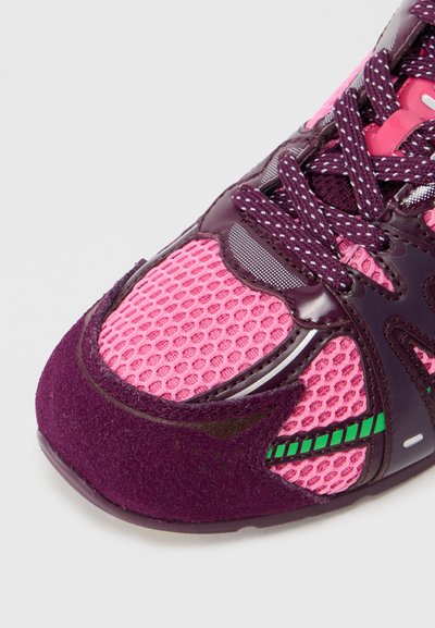 Gros plan sur une chaussure de sport rose et violette avec un tissu en maille, un embout en daim, des lacets à motifs et un accent rayé vert.
