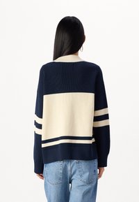 Svetr s námořnickými a krémovými pruhy se žebrovanou strukturou, širokým kulatým výstřihem a horizontálními pruhy na zádech.