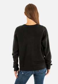 Suéter negro de punto con un corte relajado, hombros caídos y un cuello redondo. Textura suave, puños acanalados y detalles en el dobladillo.