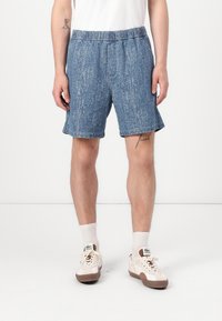Bermudas de mezclilla en azul claro con una textura sutil, que cuentan con una cintura elástica y bolsillos laterales, combinadas con calcetines deportivos blancos y zapatillas.
