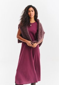Sukienka w kolorze mauve o płynnym, teksturowanym wykończeniu; nałożona na nią miękka, ciemnofioletowa szal. Prosty fason, długie rękawy i luźne dopasowanie.
