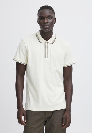 Polo shirt i lys creme, lavet af blød bomuld, med en stribet krave og tre-knap lukning. Korte ærmer med kontrasterende kanter.