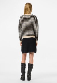 Csíkos fekete és bézs kötött pulóver kerek nyakkivágással, fekete szoknyával és térdig érő fekete csizmával, csatos részletekkel párosítva.