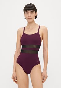 Μονοκόμματο μαγιό σε μπορντό με ρυθμιζόμενους ιμάντες, διακοσμημένο με διάφανα μαύρα διχτυωτά πάνελ στη μέση. Ομαλό ύφασμα με εφαρμοστή σχεδίαση.