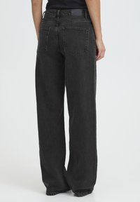 Laiade säärega mustad teksad pleekinud viimistlusega, kõrge vöökohaga, kahe tagataskuga ja diskreetse logoga vöörihma peal.