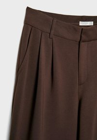 Brązowe spodnie plisowane o gładkiej fakturze, z bocznymi kieszeniami i szerokim pasem. Metka głosi "Stradivarius."