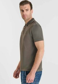 Polo de manga corta gris con cuello, que presenta un pequeño logotipo en el pecho y un ribete en contraste. Combinado con un pantalón vaquero azul.