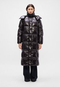 Jachetă puf cu un finisaj lucios, având un design lung și supradimensionat, model pătrățos matlasat și guler înalt.