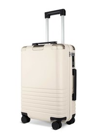 Hartschalenkoffer in Creme mit strukturierter Oberfläche, ausziehbarem Griff, vier schwarzen Rädern und einem Seitenhandle für einfaches Tragen.