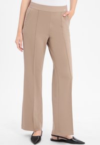 Beige weit geschnittene Hose mit einem weichen, dehnbaren Bund und ausgeprägten vorderen Nähten. Kombiniert mit schwarzen spitzen Ballerinas.
