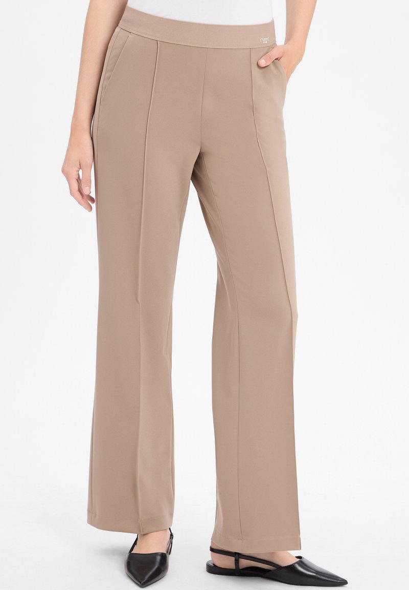 Beige weit geschnittene Hose mit einem weichen, dehnbaren Bund und ausgeprägten vorderen Nähten. Kombiniert mit schwarzen spitzen Ballerinas.