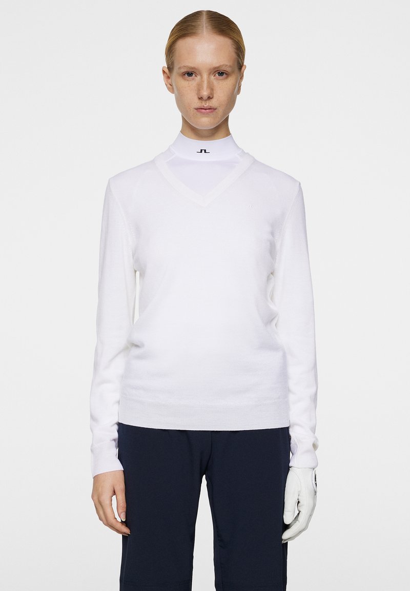 Valkoinen v-kaula-aukko kietaisu neulepaita pitkillä hihoilla, jossa on tiukka istuvuus ja ribloomit hihansuut. Yhdistetty turtleneck-paidan kanssa ja tummien housujen kanssa.
