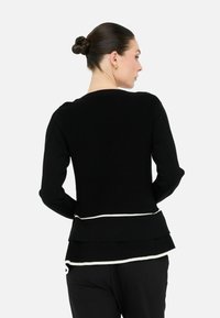 Maglione nero a maniche lunghe con texture a coste, dotato di orlo a strati e bordi bianchi, visto da dietro.