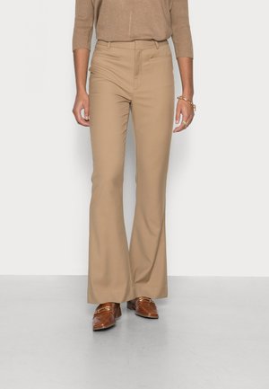 Pantalons évasés beiges en tissu lisse, dotés d'une taille ajustée et de deux poches latérales, associés à des mocassins marron.