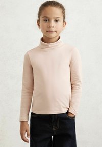 Bluză cu mânecă lungă, de culoare roz deschis, din bumbac, cu o textură moale, având un design ajustat, purtată cu blugi negri din denim, cu cusături vizibile.